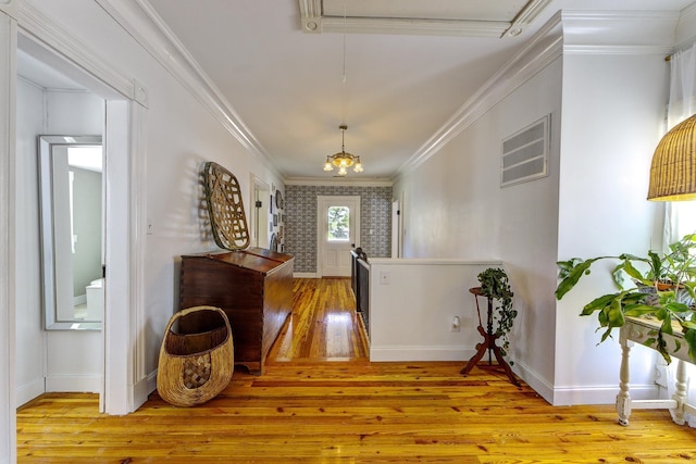 entryway with light hardwood / wood-style flooring, ornamental molding, and a notable chandelier