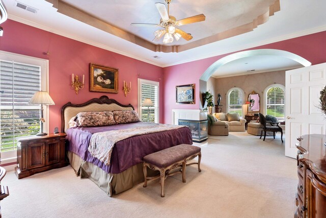 carpeted bedroom featuring ceiling fan, ornamental molding, a tray ceiling, and multiple windows