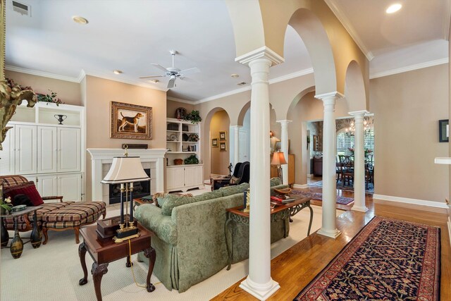 living room featuring a tiled fireplace, ornate columns, crown molding, ceiling fan, and light wood-type flooring