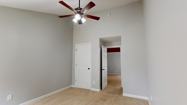 spare room featuring a high ceiling, ceiling fan, and light carpet