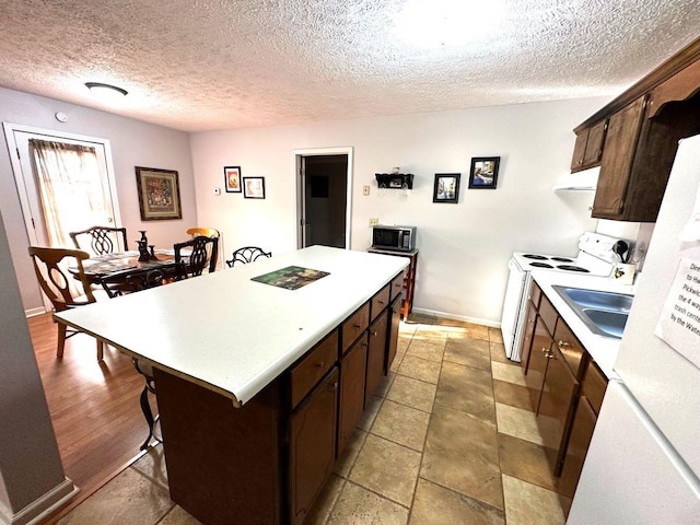 kitchen featuring a textured ceiling, a center island, dark brown cabinetry, and white range with electric cooktop