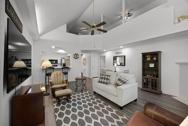 living room with dark wood-type flooring, ceiling fan, high vaulted ceiling, and a textured ceiling