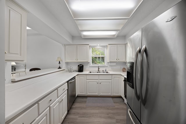 kitchen featuring hardwood / wood-style floors, kitchen peninsula, sink, appliances with stainless steel finishes, and white cabinets