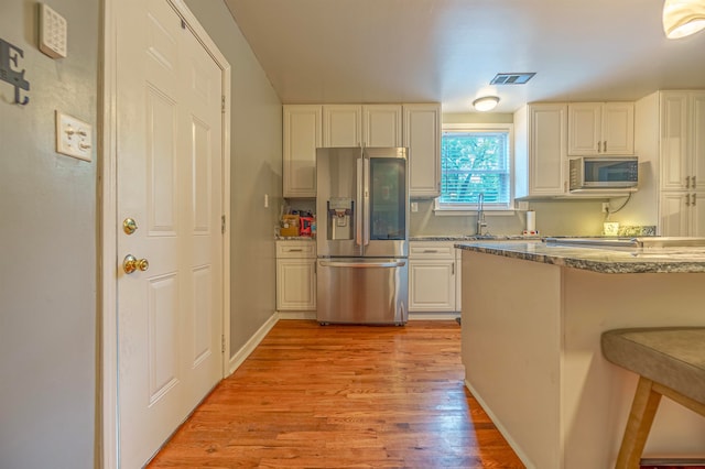 kitchen with light hardwood / wood-style flooring, appliances with stainless steel finishes, white cabinetry, kitchen peninsula, and a breakfast bar area