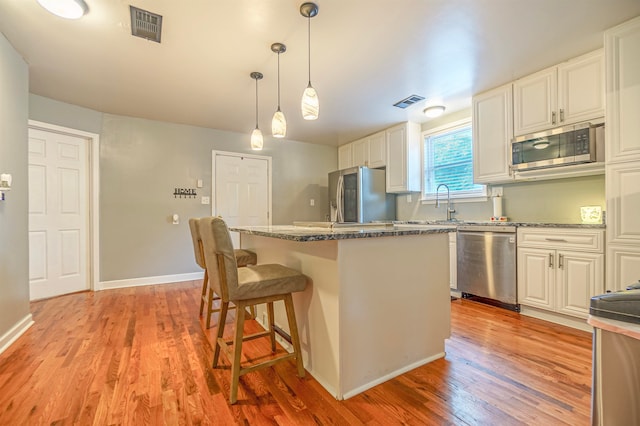 kitchen with a kitchen island, stainless steel appliances, white cabinetry, and light hardwood / wood-style flooring