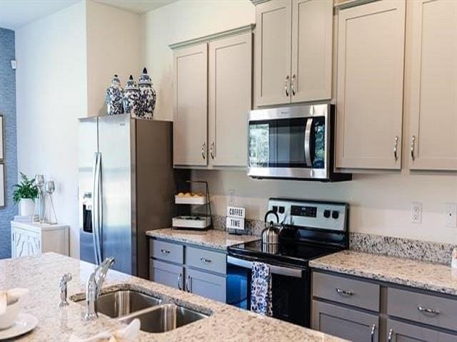 kitchen with gray cabinetry, light stone counters, stainless steel appliances, and sink