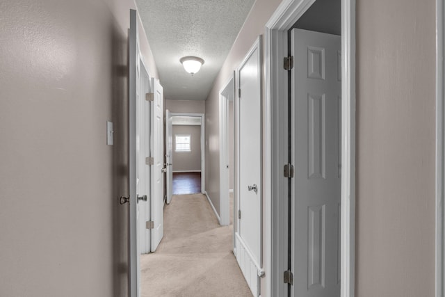 hallway featuring light colored carpet and a textured ceiling