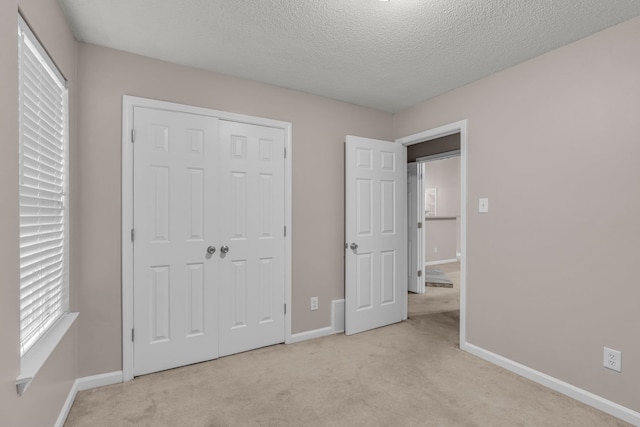 unfurnished bedroom featuring a textured ceiling, light colored carpet, and a closet