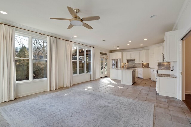 kitchen with stainless steel fridge, white cabinetry, crown molding, ceiling fan, and a kitchen island with sink