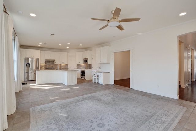 kitchen featuring ceiling fan, backsplash, white cabinetry, appliances with stainless steel finishes, and a center island