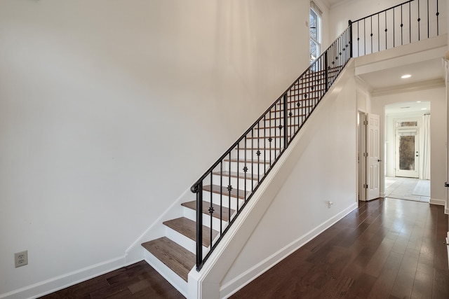 staircase with ornamental molding, a towering ceiling, and hardwood / wood-style floors