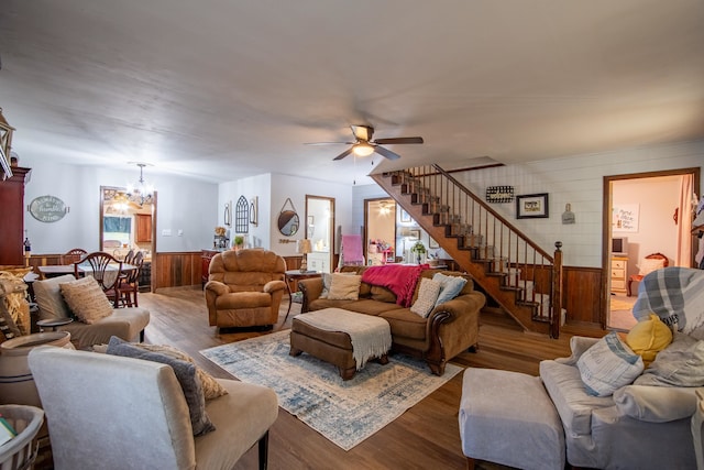 living room featuring ceiling fan with notable chandelier, wooden walls, and wood-type flooring