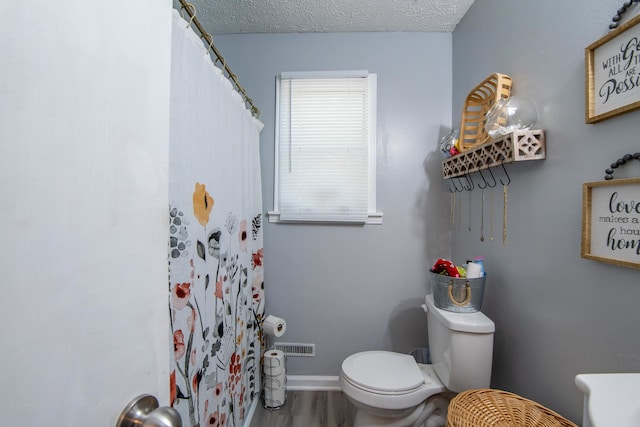 bathroom featuring walk in shower, hardwood / wood-style flooring, toilet, and a textured ceiling