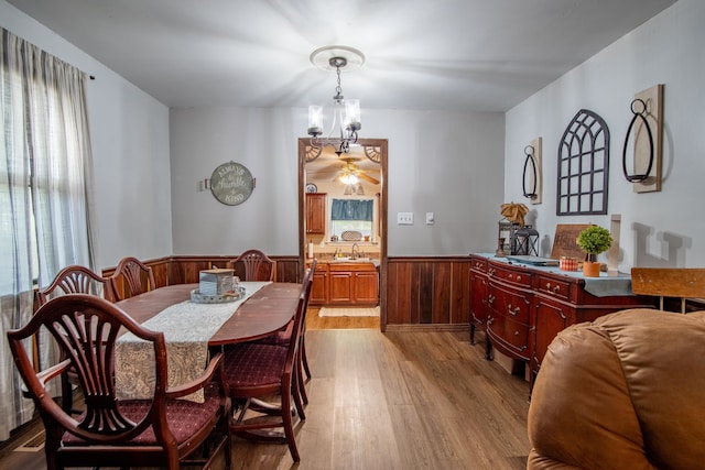 dining space featuring ceiling fan with notable chandelier, light hardwood / wood-style floors, and wooden walls