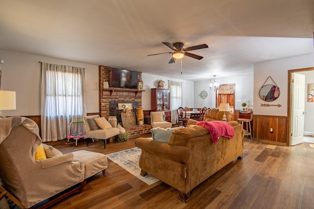 living room with ceiling fan with notable chandelier, a brick fireplace, hardwood / wood-style flooring, and wooden walls