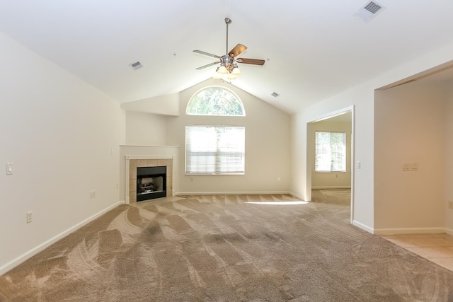 unfurnished living room featuring a healthy amount of sunlight, a tiled fireplace, ceiling fan, and light colored carpet