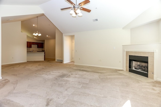 unfurnished living room with a tile fireplace, ceiling fan with notable chandelier, lofted ceiling, and light carpet