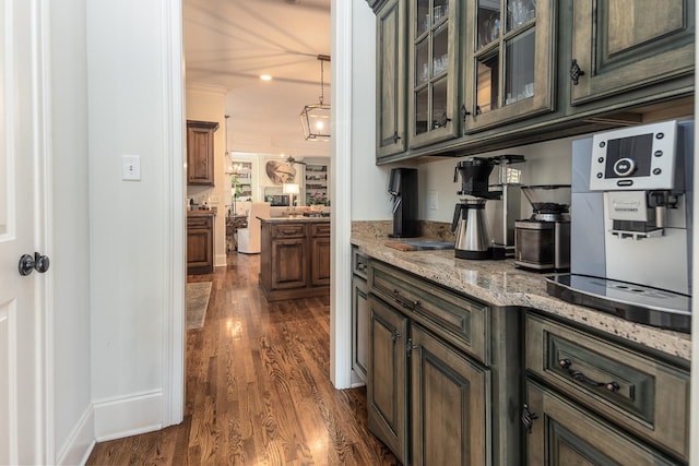 kitchen featuring pendant lighting, dark hardwood / wood-style flooring, dark brown cabinetry, crown molding, and light stone countertops