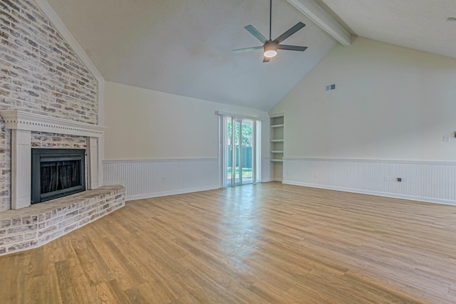 unfurnished living room featuring a brick fireplace, a textured ceiling, light hardwood / wood-style flooring, ceiling fan, and built in shelves