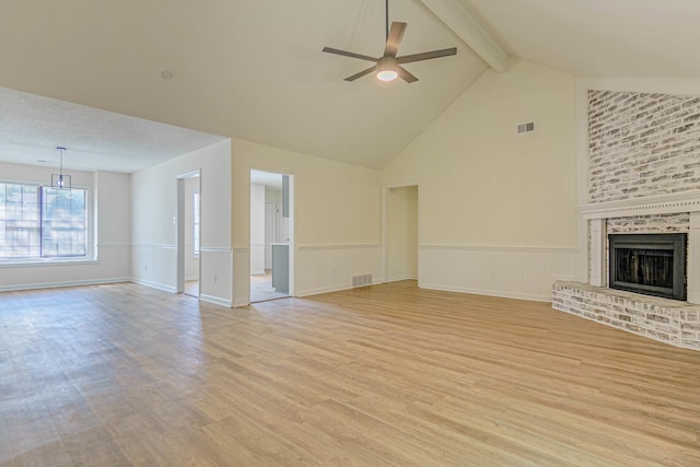 unfurnished living room featuring high vaulted ceiling, a fireplace, light wood-type flooring, beam ceiling, and ceiling fan