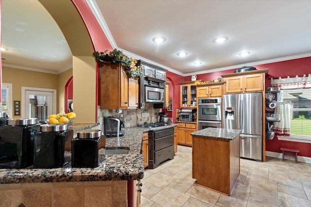 kitchen featuring tasteful backsplash, a kitchen island, appliances with stainless steel finishes, crown molding, and dark stone countertops