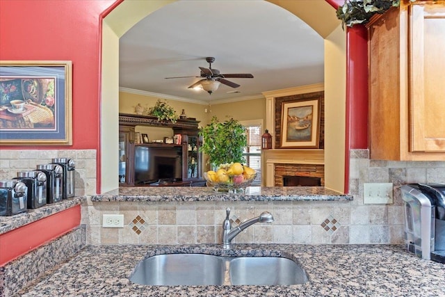 kitchen featuring decorative backsplash, a fireplace, crown molding, ceiling fan, and sink