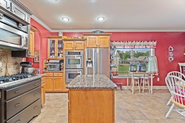 kitchen with appliances with stainless steel finishes, tasteful backsplash, a center island, dark stone counters, and ornamental molding