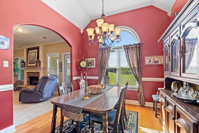 dining area featuring light wood-type flooring, a chandelier, vaulted ceiling, a fireplace, and crown molding