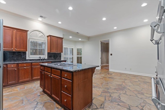 kitchen featuring ornamental molding, a kitchen island, stainless steel gas cooktop, dark stone counters, and decorative backsplash