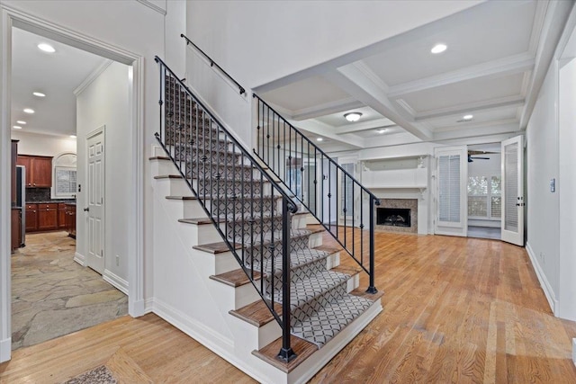 staircase with coffered ceiling, beamed ceiling, wood-type flooring, ceiling fan, and a premium fireplace