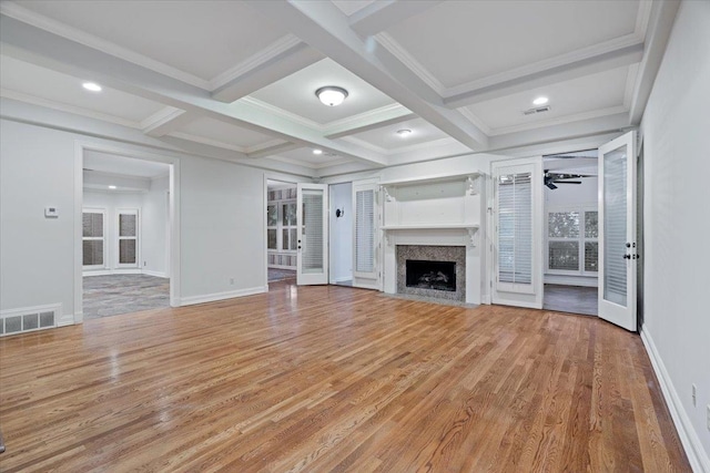 unfurnished living room featuring ceiling fan, beamed ceiling, a premium fireplace, coffered ceiling, and light hardwood / wood-style floors