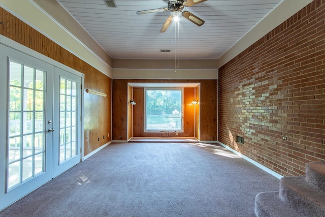 unfurnished room with ceiling fan, wooden walls, plenty of natural light, and french doors