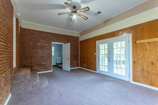 unfurnished bedroom with wooden walls, carpet, ceiling fan, brick wall, and french doors