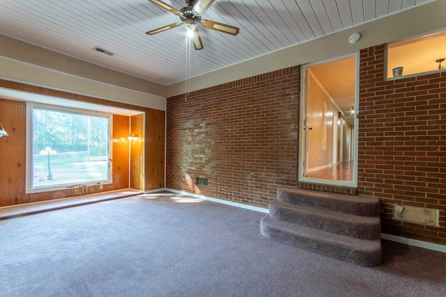 unfurnished living room with ceiling fan, carpet floors, and brick wall