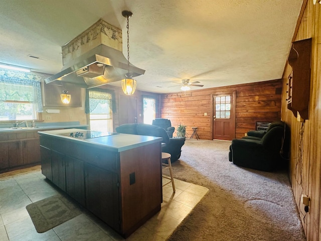 kitchen with wood walls, a kitchen island, a textured ceiling, ceiling fan, and light colored carpet