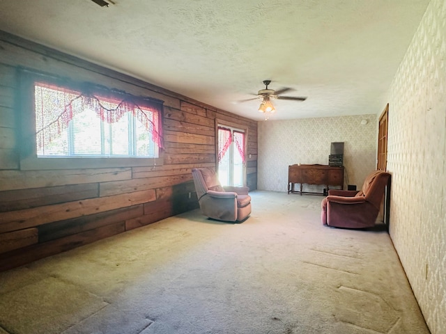 living area featuring a textured ceiling, carpet, wood walls, and ceiling fan