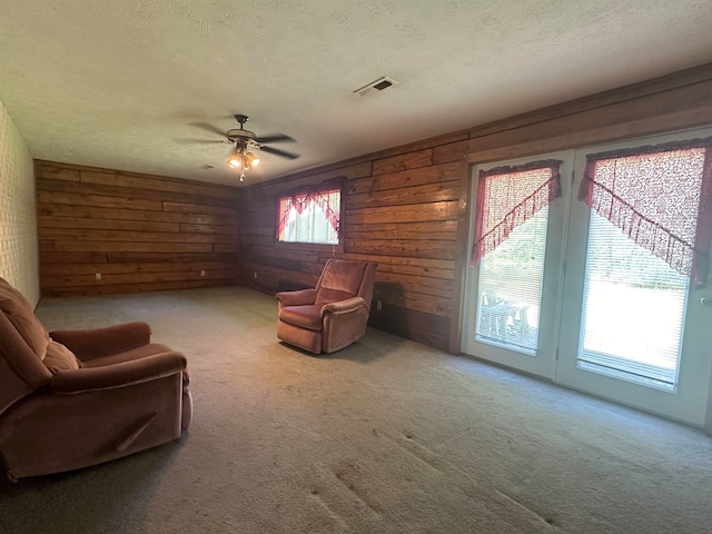 living room with wood walls, ceiling fan, carpet flooring, and a textured ceiling