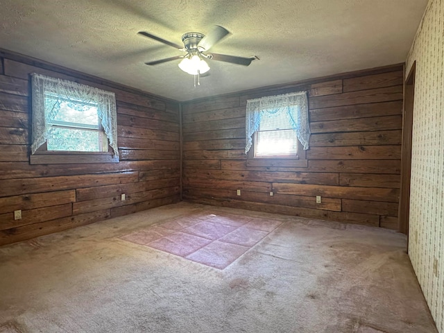 spare room with a textured ceiling, carpet flooring, wooden walls, and ceiling fan