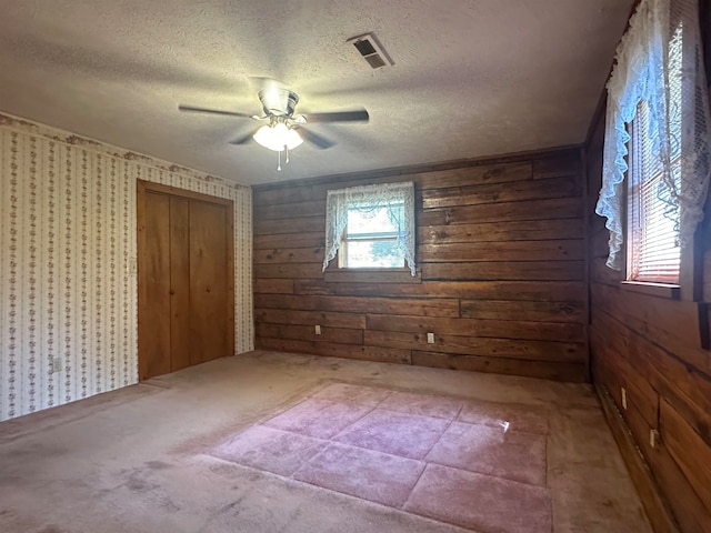 unfurnished bedroom featuring a textured ceiling, wood walls, ceiling fan, and a closet