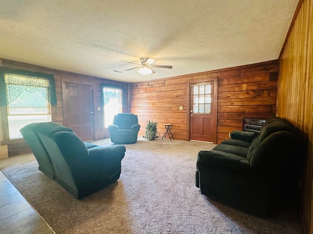 carpeted living room with wooden walls, ceiling fan, and a wealth of natural light