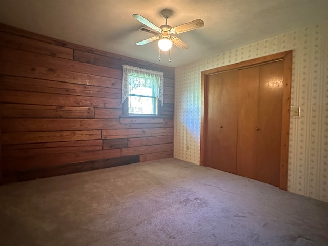 unfurnished bedroom with carpet, wood walls, ceiling fan, and a closet