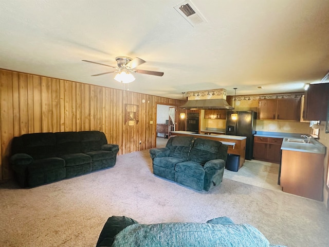 carpeted living room with wood walls, ceiling fan, and sink