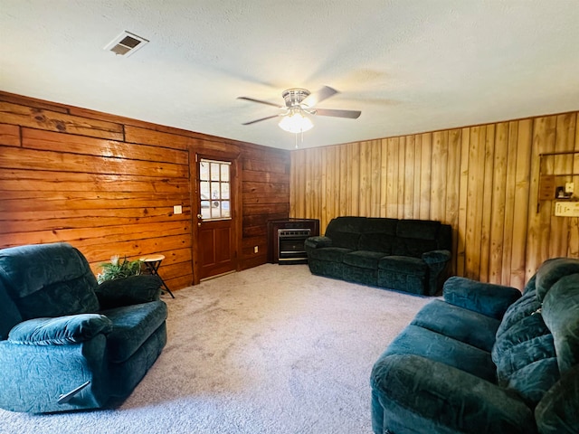 carpeted living room featuring a textured ceiling, wood walls, and ceiling fan