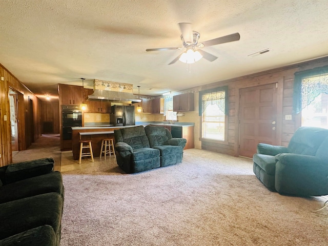 carpeted living room with a textured ceiling, wood walls, and ceiling fan