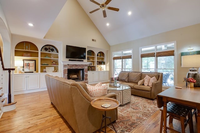 living room featuring a brick fireplace, ceiling fan, high vaulted ceiling, and light wood-type flooring