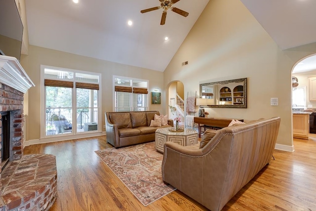 living room featuring ceiling fan, a fireplace, high vaulted ceiling, and light hardwood / wood-style flooring