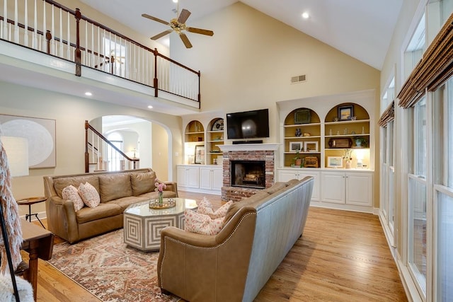 living room with ceiling fan, light hardwood / wood-style flooring, high vaulted ceiling, and a brick fireplace