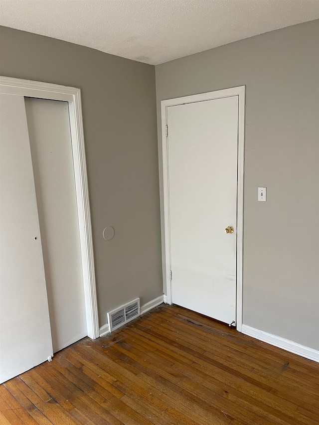 unfurnished bedroom featuring a closet, a textured ceiling, and dark hardwood / wood-style floors