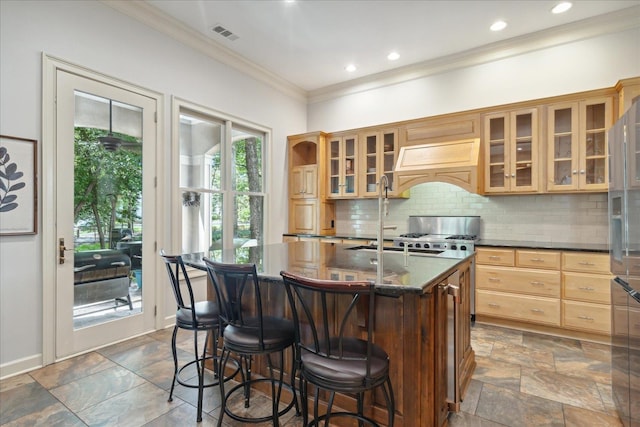 kitchen featuring decorative backsplash, a center island with sink, dark stone counters, ornamental molding, and sink