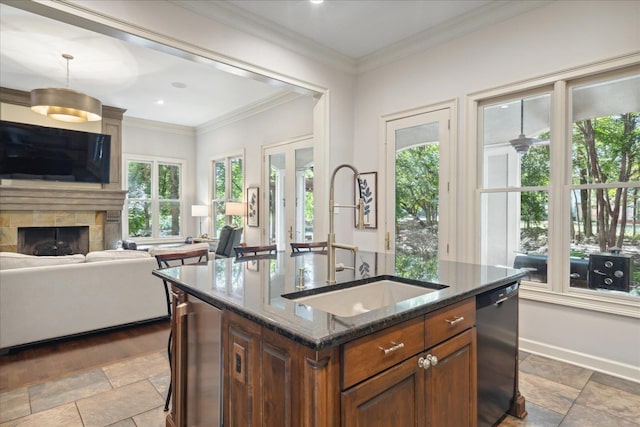 kitchen featuring an island with sink, a stone fireplace, black dishwasher, dark stone counters, and sink